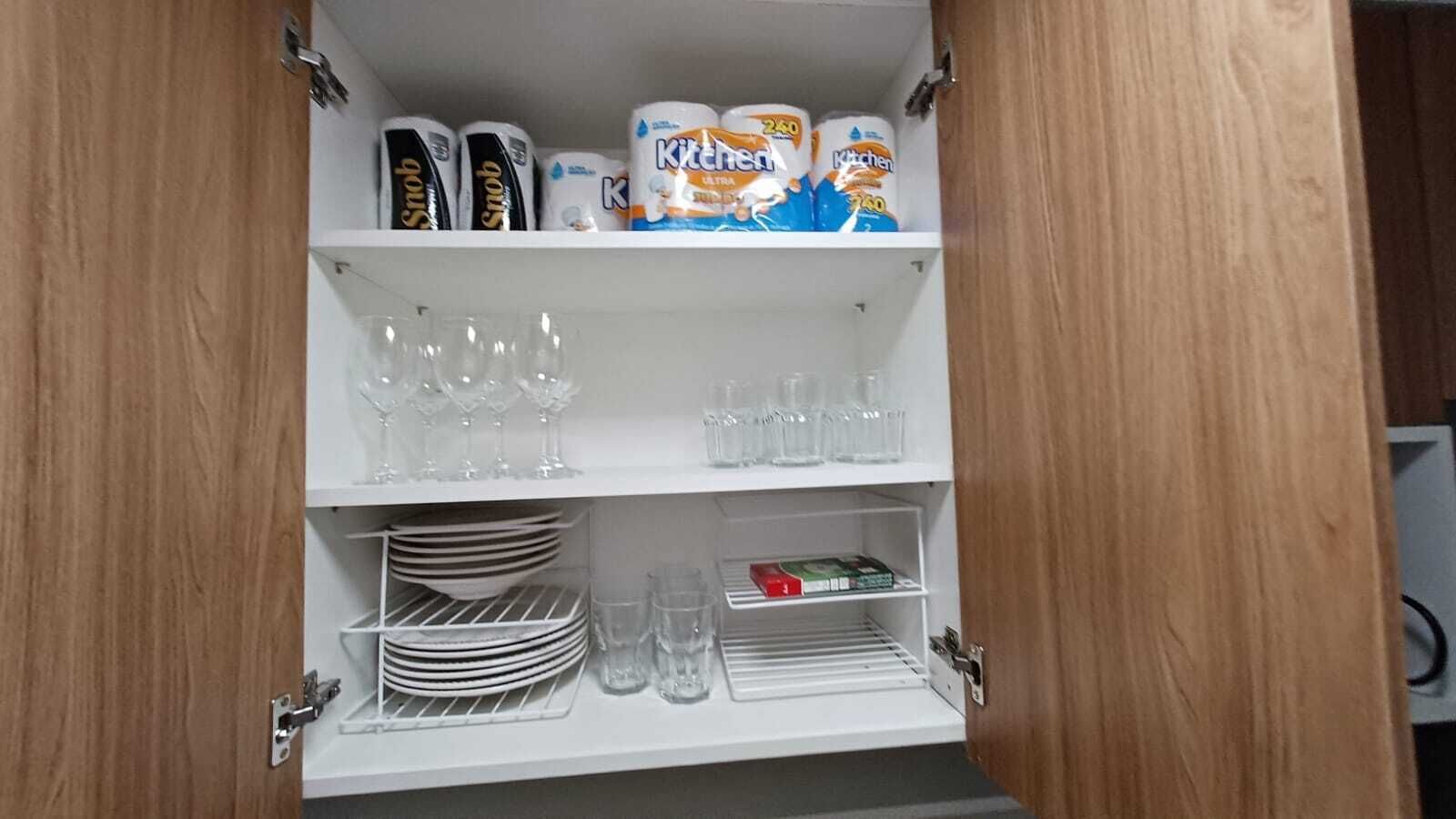 Un armario de cocina con estantes que contiene papel higiénico, cristalería y platos.