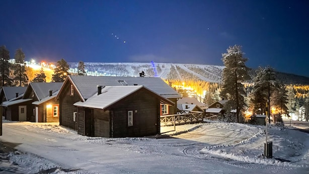A snow-covered village with wooden cabins, a ski lift, and a mountain in the background.