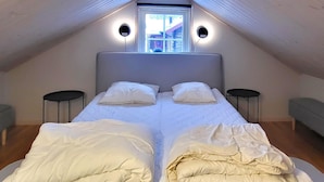 A bedroom with a large bed, two bedside tables, a window, and a sloped ceiling.