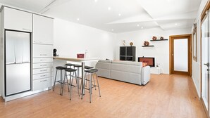 Ett modernt kök med kylskåp, barstolar, ett matbord och en grå soffa.