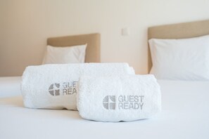 A bed with two white towels on it, each with 'GUEST READY' embroidered on them.