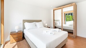 Ett hotellrum med en säng, träbord som sängbord, en stor spegel och utsikt över grönområden utanför.