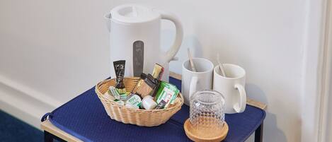 A small table with a basket of toiletries, a coffee maker, and two white mugs.