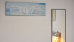Una pintura de un edificio en una pared, un espejo y una mesita de noche con una lámpara.