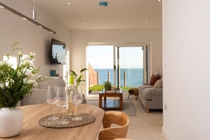 Ein modernes Wohnzimmer mit einem Esstisch, Stühlen und Meerblick durch große Glasüren.