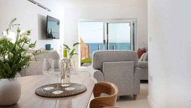 A modern living room with a dining area, a television, and a view of the sea.