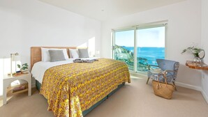 A bedroom with a bed, a chair, a small table, and a view of the ocean.