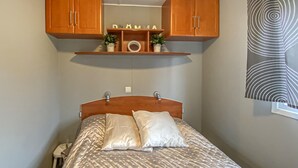 Ein Schlafzimmer mit einem Bett, Holzschränken darüber, einem Regal mit Dekoration und einem Fenster mit einem gemusterten Vorhang.