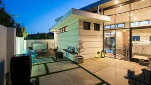 A modern house with a patio area, outdoor seating, and a glass door leading to a kitchen. - Hollywood Hills - Universal Studios- 4Bedroom- Sunset Views!!! (Los Angeles)