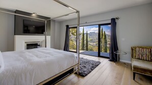 A bedroom with a bed, a TV, a fireplace, a balcony with curtains, and a view of trees and mountains. - Hollywood Hills - Universal Studios- 4Bedroom- Sunset Views!!! (Los Angeles)