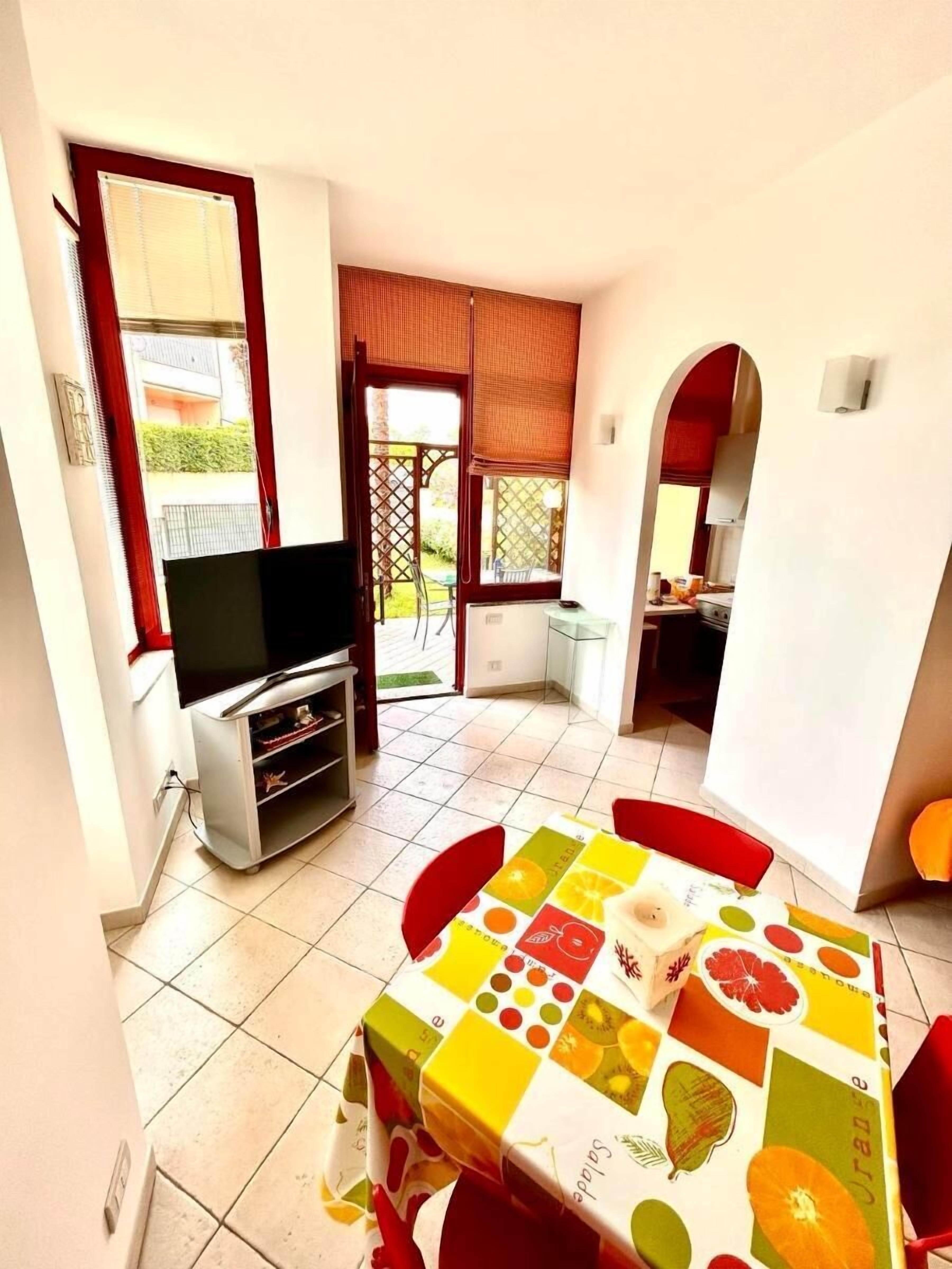 A dining area with a table set for two, a television, and a kitchen visible through an open door.