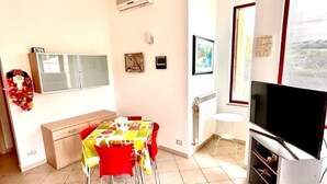 A dining area with a table and chairs, a television, and a radiator. - TRILO OSIMO MARCELLI - Delightful three-room apartment with garden near the sea (Marcelli)