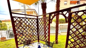 A covered patio with a table and chairs, surrounded by a lattice fence, and a view of buildings in the background. - TRILO OSIMO MARCELLI - Delightful three-room apartment with garden near the sea (Marcelli)