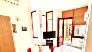 A dining area with a table and chairs, a television, and a view of the outside. - TRILO OSIMO MARCELLI - Delightful three-room apartment with garden near the sea (Marcelli)