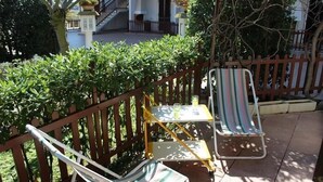 Uma varanda com duas poltronas de descanso, uma pequena mesa e um cercado de madeira.