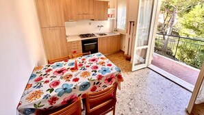 A compact kitchen with wooden cabinets, a gas stove, and a dining table with a floral tablecloth. - TRILO EUGENIO MARCELLI - Comfortable three-room apartment with a/c near the sea (Marcelli)