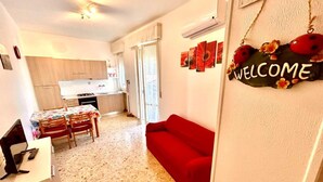 A compact living space with a kitchenette, a dining area, and a red sofa. - TRILO EUGENIO MARCELLI - Comfortable three-room apartment with a/c near the sea (Marcelli)