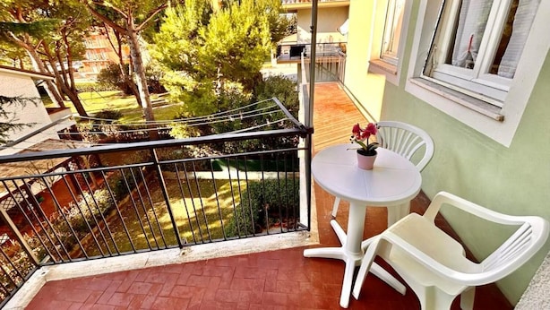 A balcony with a table and chairs, a potted plant, and a view of trees and buildings. - TRILO EUGENIO MARCELLI - Comfortable three-room apartment with a/c near the sea (Marcelli)