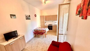 A compact living space with a kitchenette, a dining area, and a seating area with a red sofa. - TRILO EUGENIO MARCELLI - Comfortable three-room apartment with a/c near the sea (Marcelli)