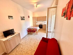 Un espacio habitable compacto con kitchenette, comedor y zona de estar con sofá rojo.