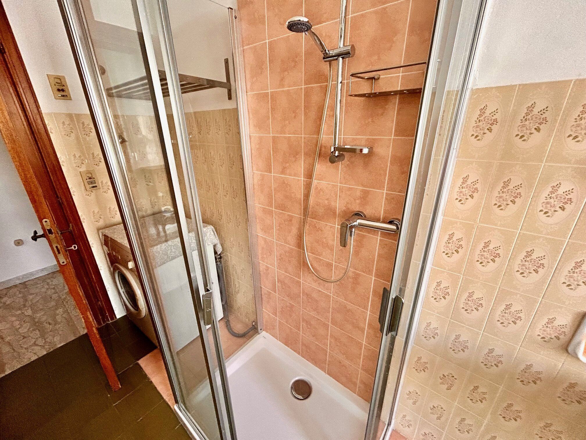 A glass-enclosed shower with a handheld showerhead, a wall-mounted faucet, and a shower control panel.