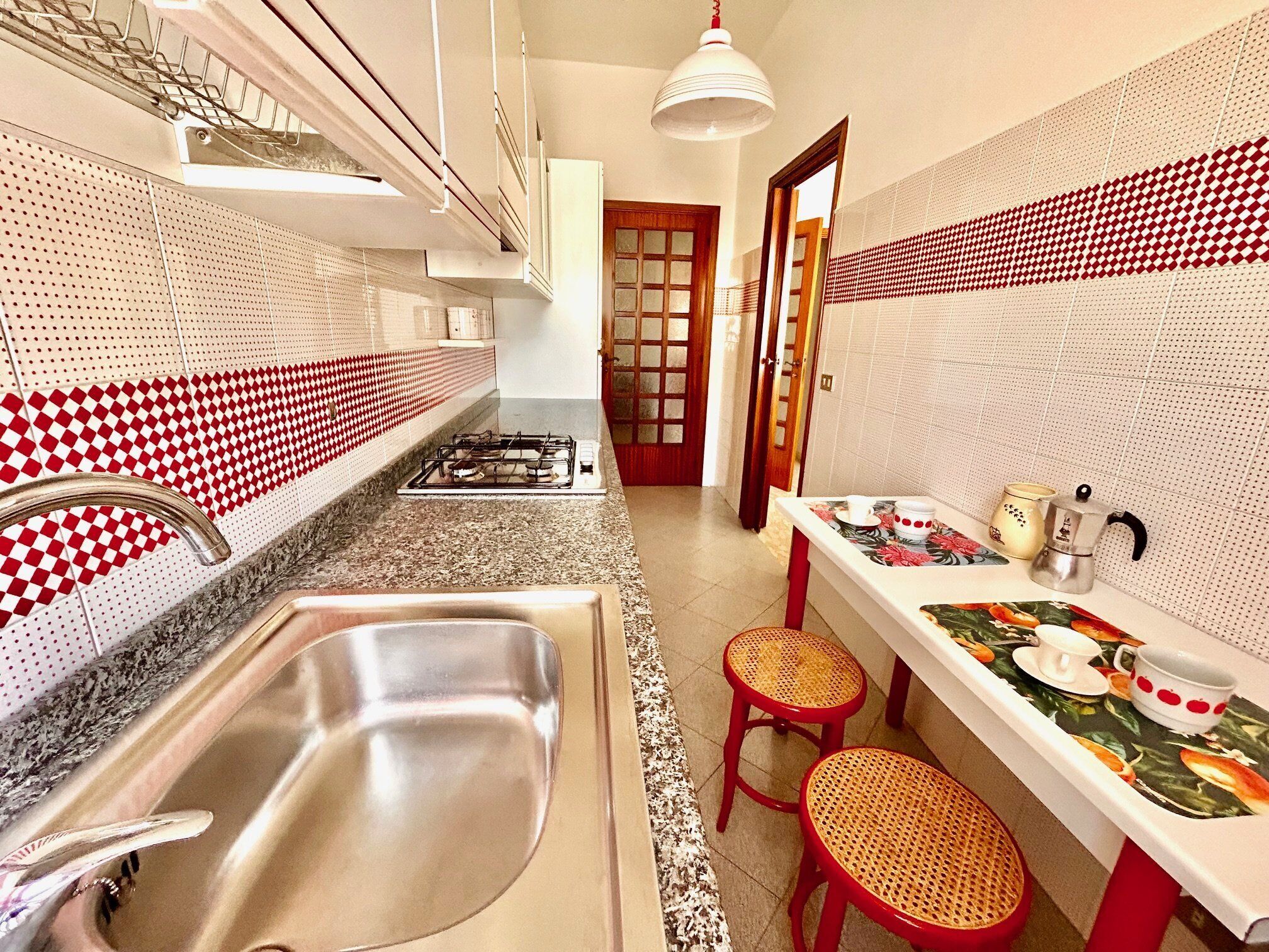 Cocina con estufa a gas, pileta y taburetes rojos.