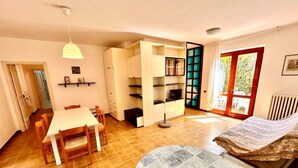 Una stanza con un tavolo da pranzo, sedie, un divano, una libreria e una finestra.