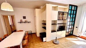 Una stanza con un tavolo da pranzo, sedie, un armadietto bianco e una televisione.