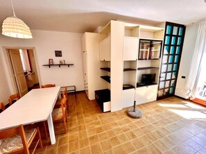 A room with a dining table, chairs, a white cabinet, and a television. - TRILO FRAU NUMANA - Lovely three-room apartment with outdoor space and two bathrooms (Sirolo)