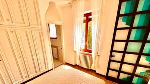 Una stanza con una grande finestra, un termosifone e una porta con un pannello di vetro.
