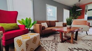 Una sala de estar con un sofá rojo, un sofá marrón, una mesa de centro de madera y un reposapiés estampado.
