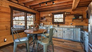 A rustic wooden cabin interior with a dining area, kitchen, and large windows. - Makin' Memories Cabin | Hot Tub, Views, Loft, Fire Pit & Game Area + FREE  Tickets (Sevierville)