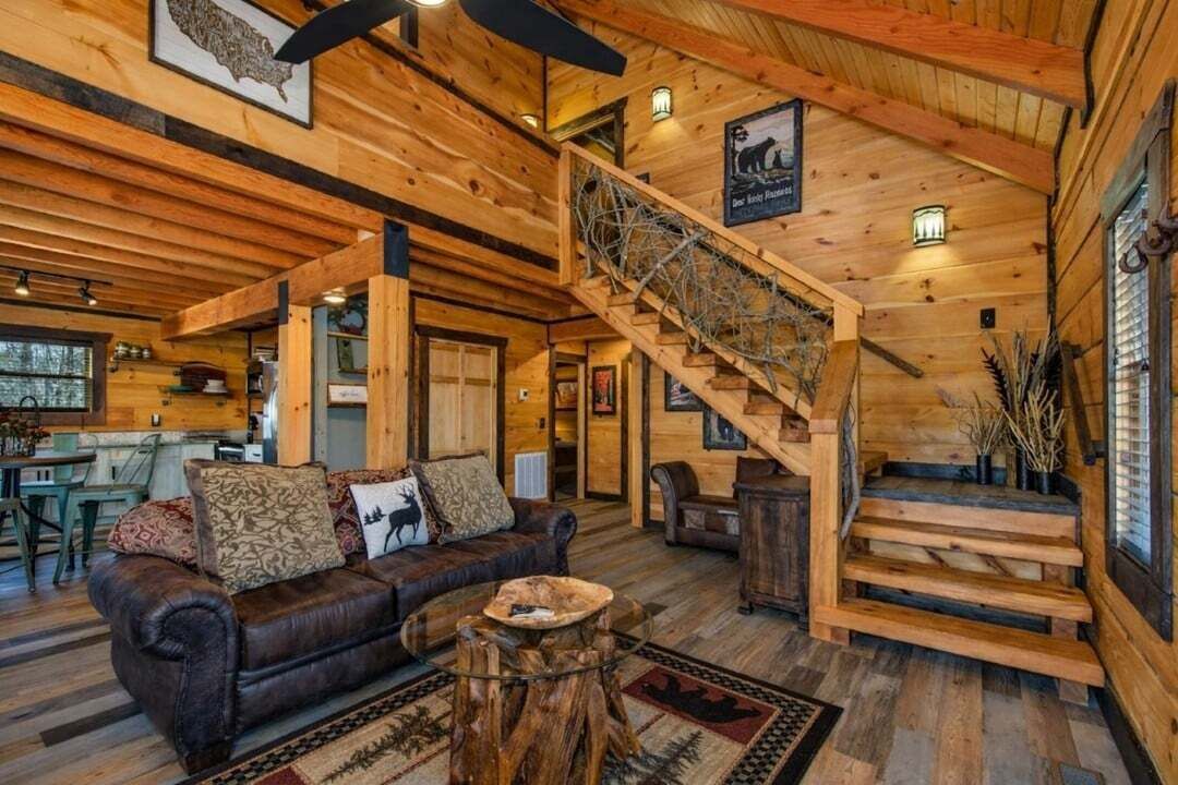 A wooden cabin interior with a staircase, a leather sofa, and a dining area.