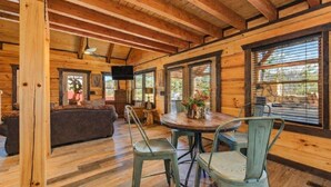 A wooden cabin interior with a dining area, a sofa, and a television. - Makin' Memories Cabin | Hot Tub, Views, Loft, Fire Pit & Game Area + FREE  Tickets (Sevierville)