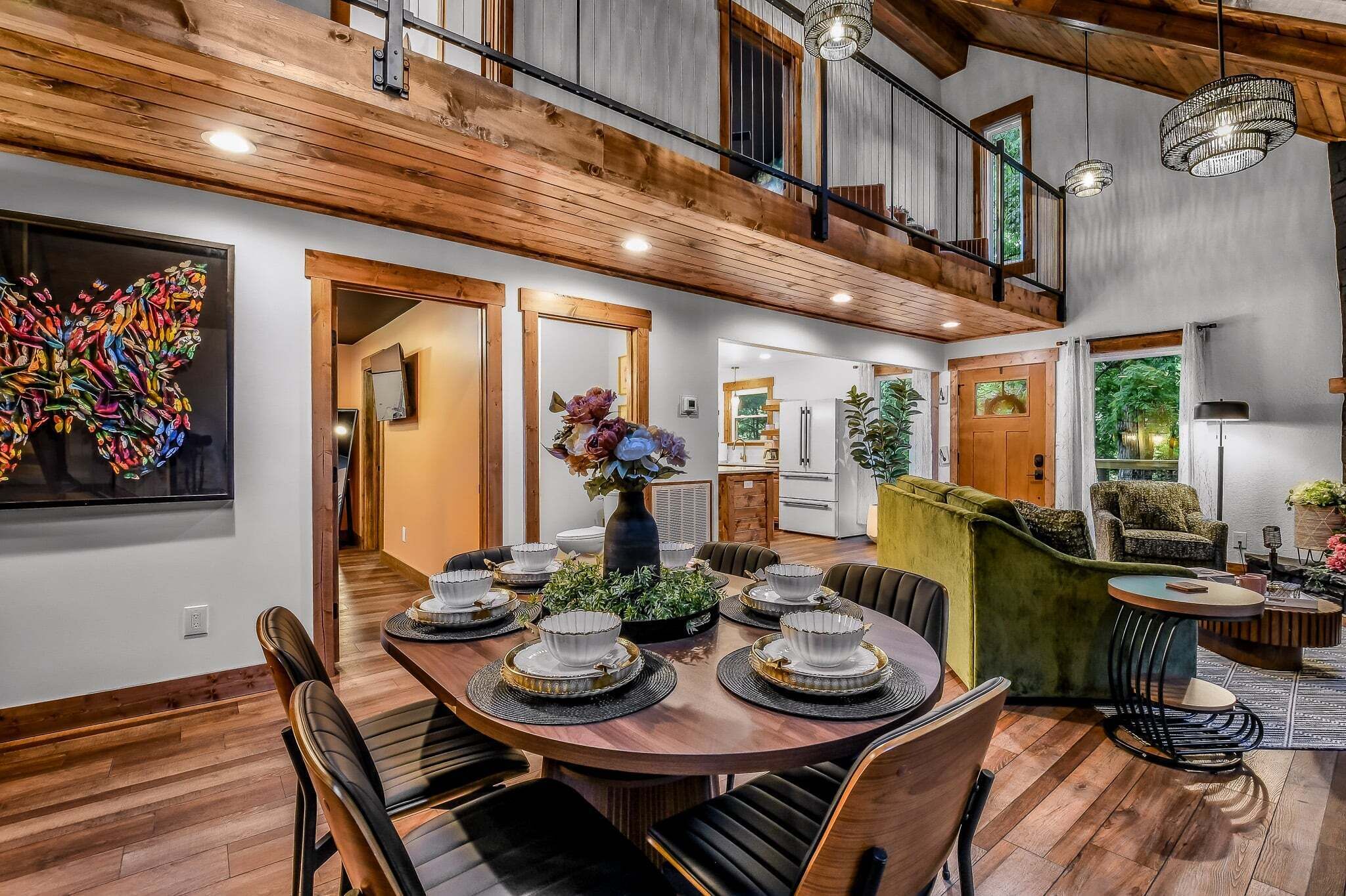 Un comedor con una mesa de madera preparada para seis personas, rodeada de sillas, un sofá verde y una pequeña mesa redonda con una lámpara.