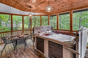 Eine Holzterrasse mit Whirlpool, Tisch und Stühlen sowie Blick auf den Wald.