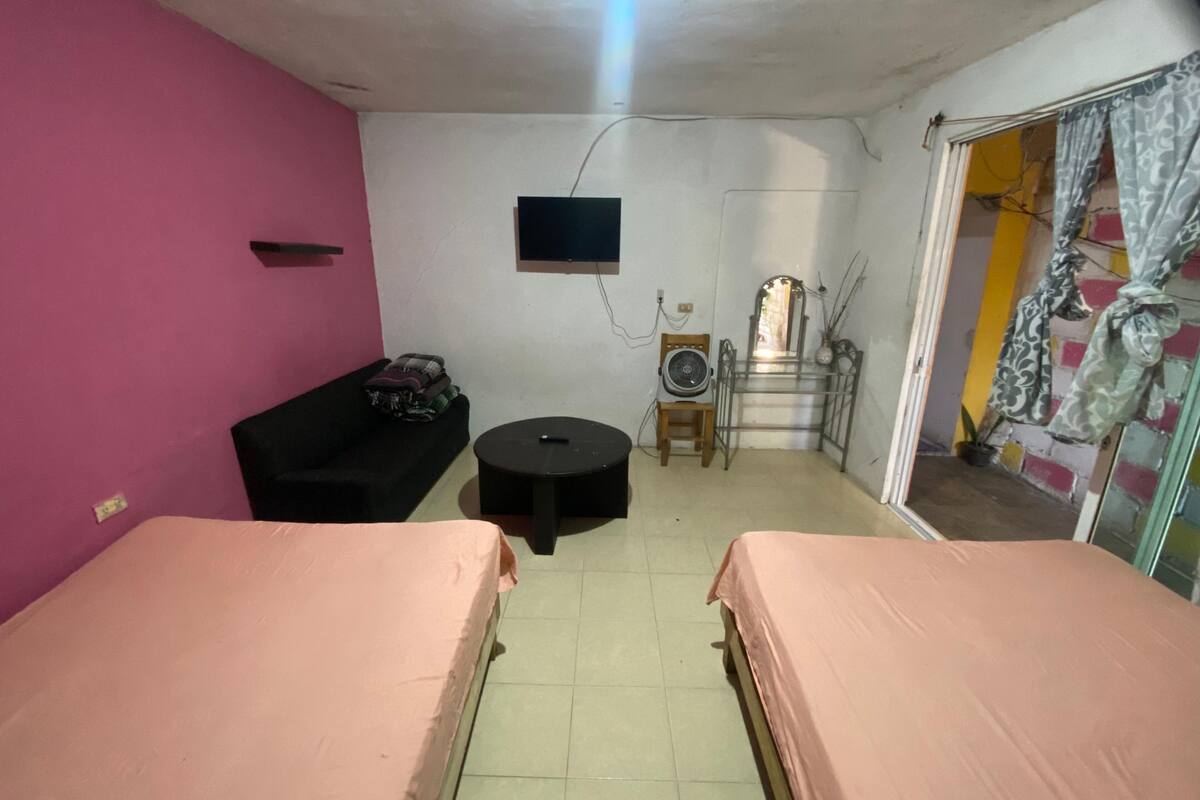 Een kamer met twee bedden, een tafeltje, een stoel, een televisie en een ventilator.