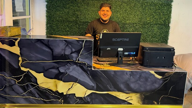 A person at a desk with a Sceptre computer, a black and gold marble-patterned table, and a green wall with a plant. - HOTEL Y PIZZERIA CASA INN (Xalapa)