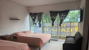 A room with two beds, a sofa, a window with curtains, and a view of a yellow building. - HOTEL Y PIZZERIA CASA INN (Xalapa)