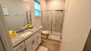 A bathroom with a granite countertop sink, a toilet, and a glass-enclosed shower. - 1120-Spacious 4BR All Suites - 20 min to Disney (Kissimmee)
