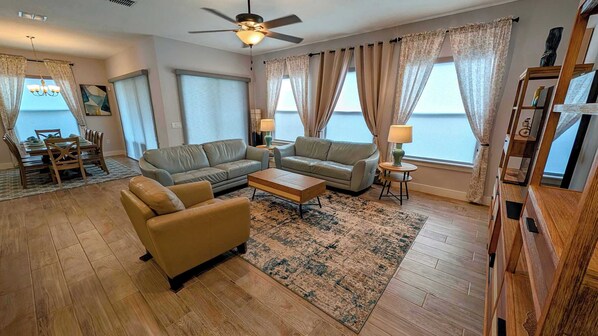 A living room with a sofa, armchair, coffee table, and a ceiling fan. - 1120-Spacious 4BR All Suites - 20 min to Disney (Kissimmee)