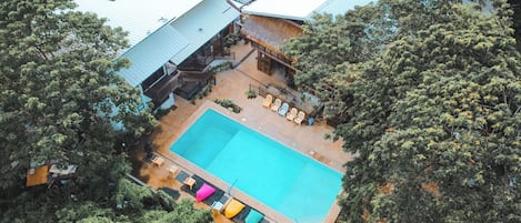 An aerial view of a resort with a swimming pool, lounge chairs, and a building with a blue roof.