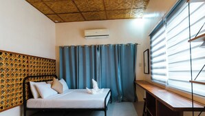 Un dormitorio con cama, cabecera de madera, ventana con persianas y equipo de aire acondicionado.