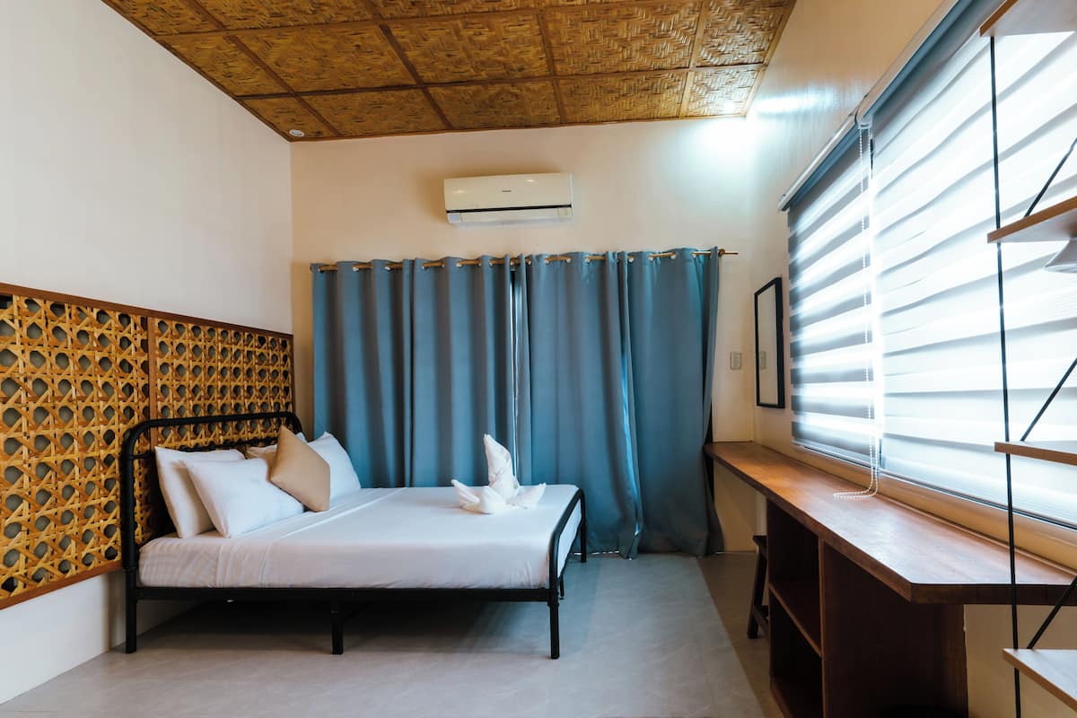 A bedroom with a bed, a wooden headboard, a window with blinds, and an air conditioning unit.
