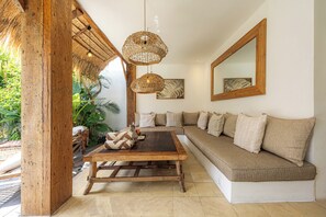 A cozy living area with a wooden coffee table, a sofa with cushions, a hanging wicker light fixture, and a large mirror on the wall. - Luxury 3BR Mediterranean Villa w/ Bfast & Butler (Badung)