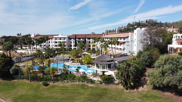 Een resort met een zwembad, palmbomen en uitzicht op het omliggende landschap.