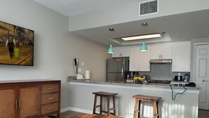 Een moderne keuken met een inbouwkoelkast, een magnetron en een fornuis. Er is een eethoek met een houten tafel en twee barkrukken.