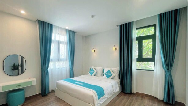 A modern hotel room with a bed, a bedside table, a mirror, and a window with curtains. - Win House Hotel (Phu Quoc)