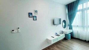 A modern room with a white wall, a mounted TV, a small white console table, a blue trash bin, and a window with blue curtains. - Win House Hotel (Phu Quoc)