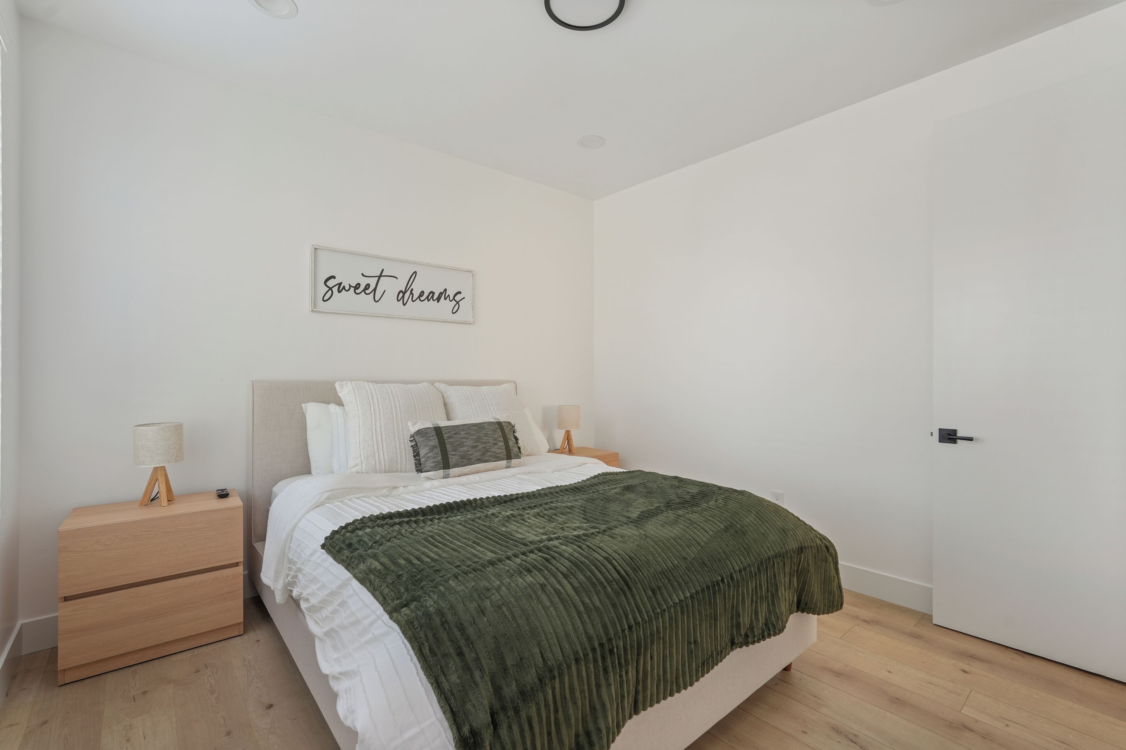 A bedroom with a bed, nightstands, a wall-mounted lamp, a door, and a wall sign.